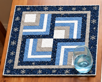 Frosted Snowflake Log Cabin winter placemat with a water glass, showing four Log Cabin blocks rotated into a pinwheel