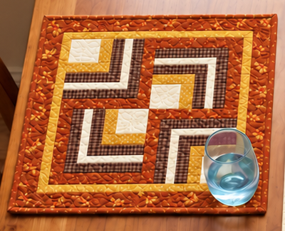 Harvest Hearth Log Cabin fall placemat with a water glass, showing four Log Cabin blocks rotated into a pinwheel