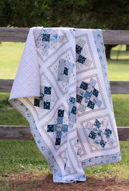 Scrappy Patchwork quilt pattern draped over a wooden fence in a country garden