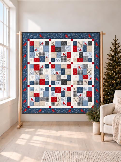 Cardinal Snowfall 10-inch square quilt pattern PDF, winter cardinal throw quilt in blue, red and white on a wooden stand in a bright room
