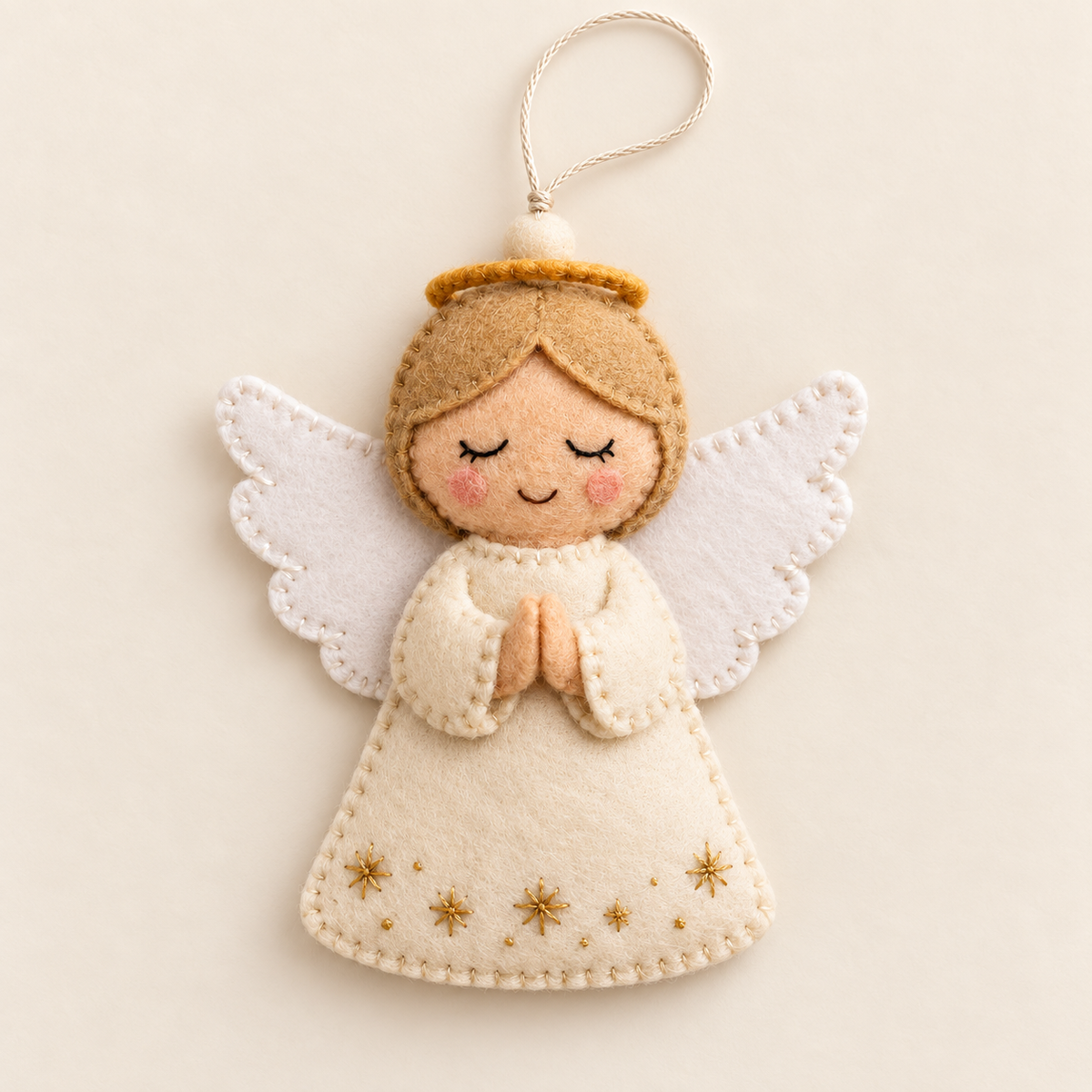 Cream felt angel ornament with white wings and gold stars on an ivory background