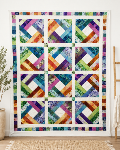 Diamond Log Cabin quilt displayed on a white wall in a modern living room with olive plant, wooden ladder, and woven rug – colorful batik patchwork home decor