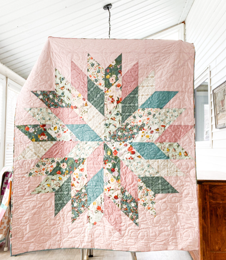 Floral Star quilt hanging display showing real finished quilt – pink and teal modern star patchwork PDF pattern for beginners