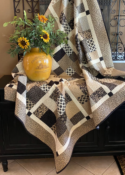 Layer Cake Toss Quilt draped over furniture – handmade patchwork throw quilt in brown and cream batik prints