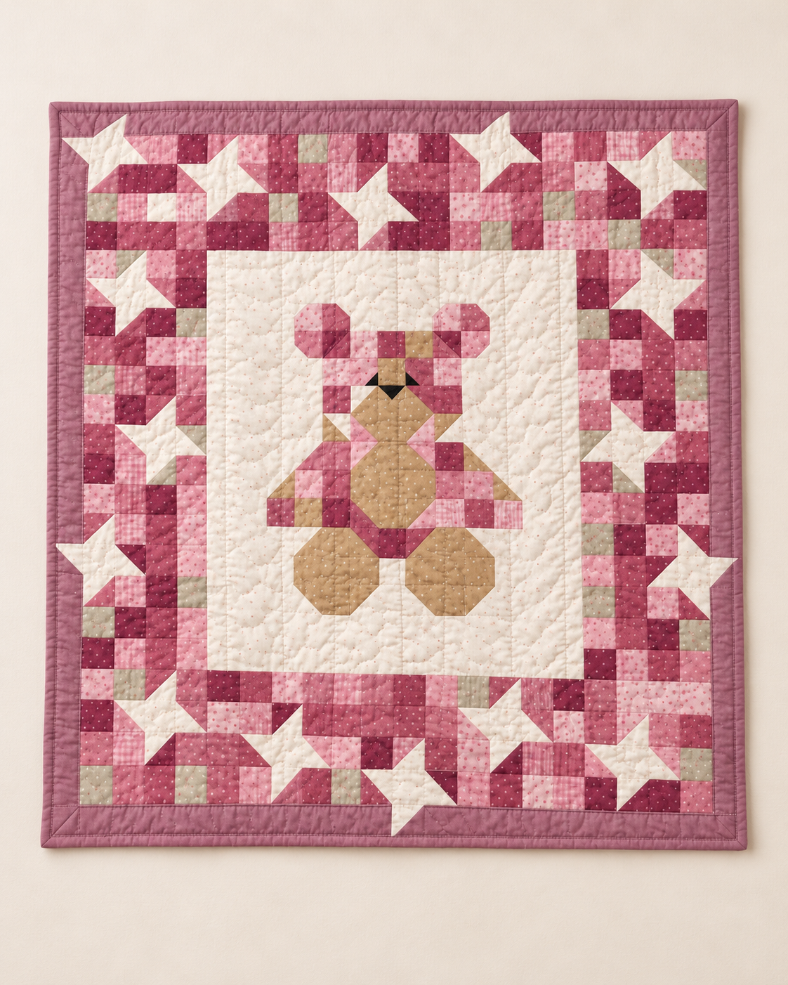 Full view of the pink teddy bear baby quilt with an ivory center panel, a starry pink patchwork frame and a mauve border